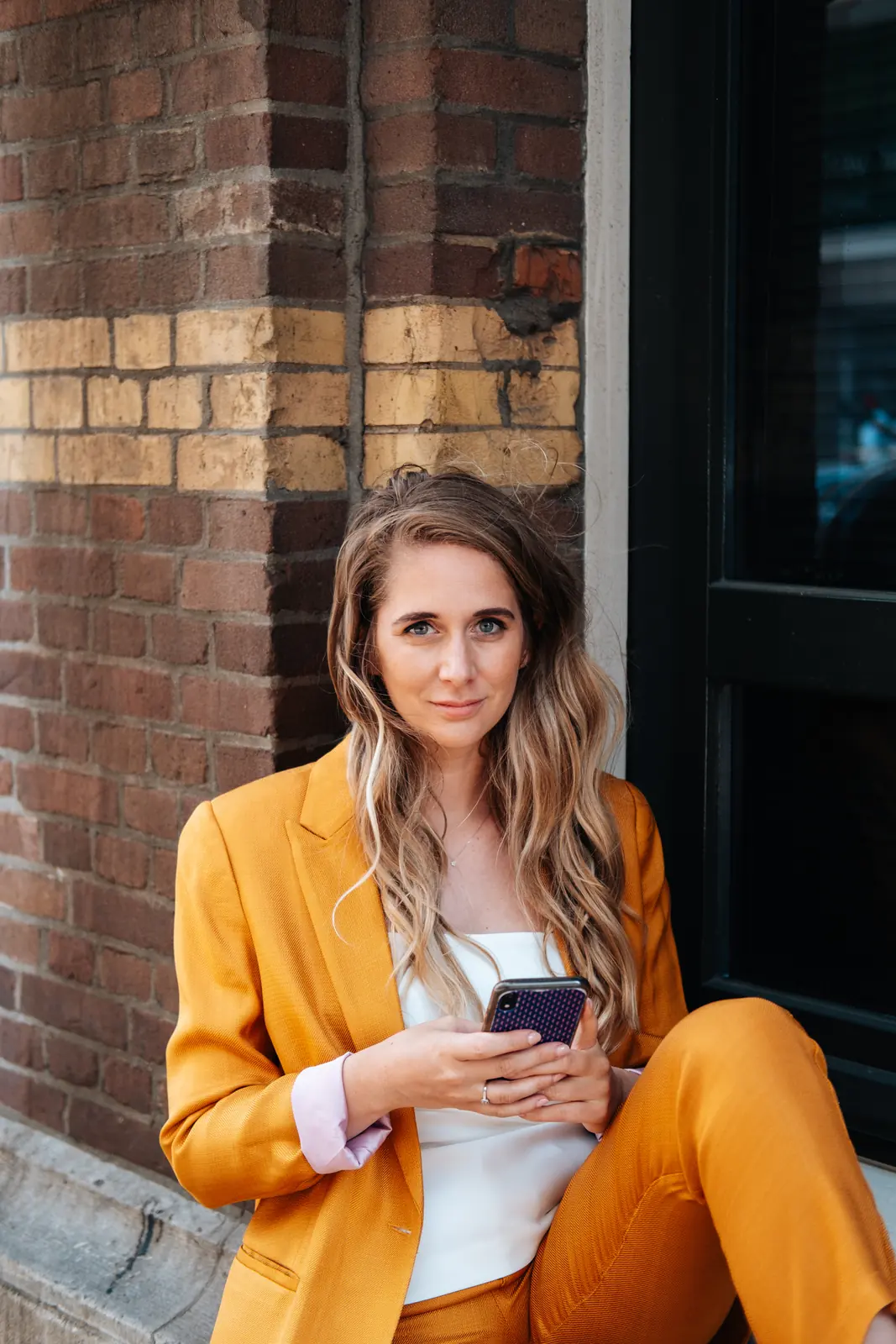 Carlijn Bekker, social media strateeg, in een oranje pak voor een bakstenen gevel