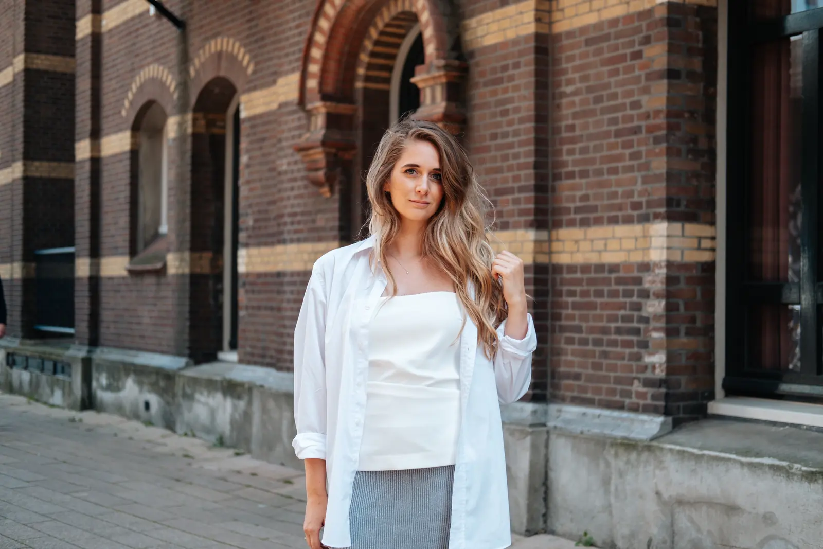 Carlijn Bekker, social media strateeg, in een wit overhemd voor een bakstenen gevel