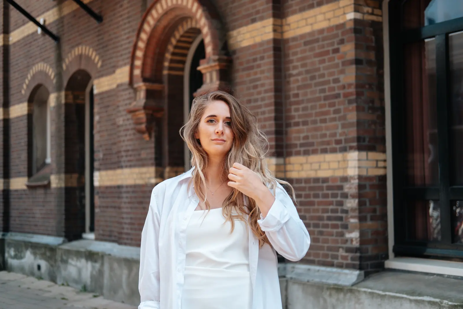 Carlijn Bekker, social media strateeg, in een wit overhemd voor een bakstenen gevel